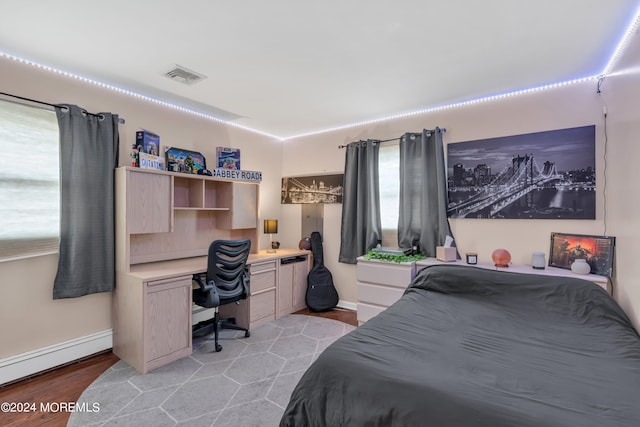 bedroom featuring light hardwood / wood-style floors, built in desk, and a baseboard heating unit