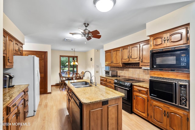 kitchen with decorative backsplash, a center island with sink, black appliances, light hardwood / wood-style floors, and sink