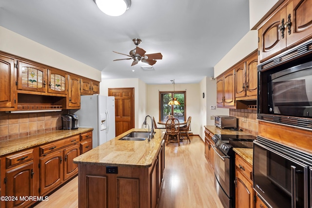 kitchen featuring tasteful backsplash, black appliances, sink, light hardwood / wood-style flooring, and a kitchen island with sink