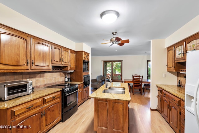 kitchen with a kitchen island with sink, light hardwood / wood-style flooring, backsplash, sink, and black appliances