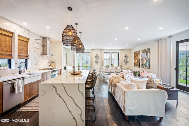 interior space with a wealth of natural light, a kitchen island, wall chimney range hood, and stainless steel appliances