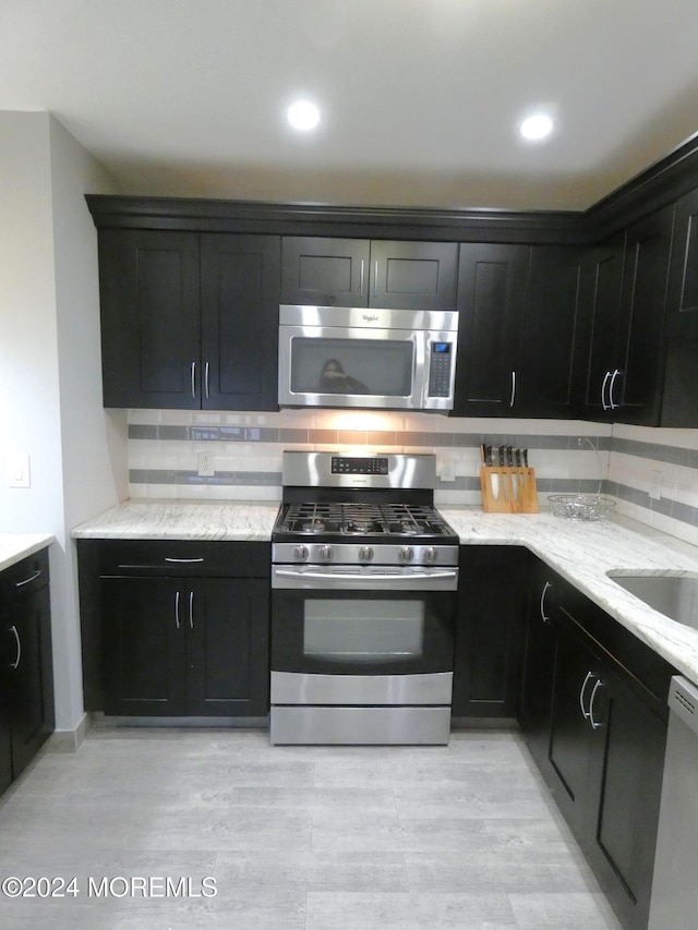 kitchen with stainless steel appliances, light stone counters, light hardwood / wood-style floors, and tasteful backsplash