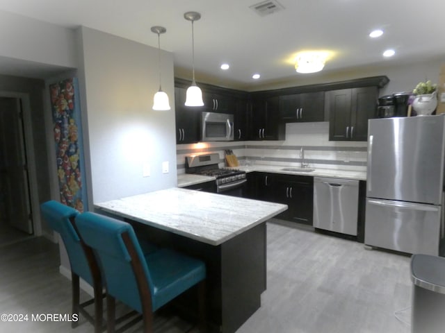 kitchen featuring light hardwood / wood-style floors, sink, appliances with stainless steel finishes, a kitchen bar, and pendant lighting