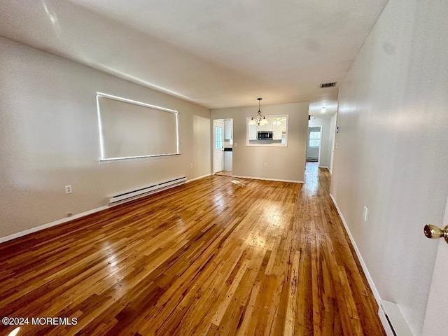 unfurnished living room featuring hardwood / wood-style flooring, a baseboard heating unit, and a chandelier