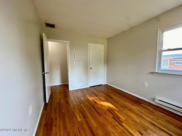 unfurnished bedroom with baseboard heating and wood-type flooring