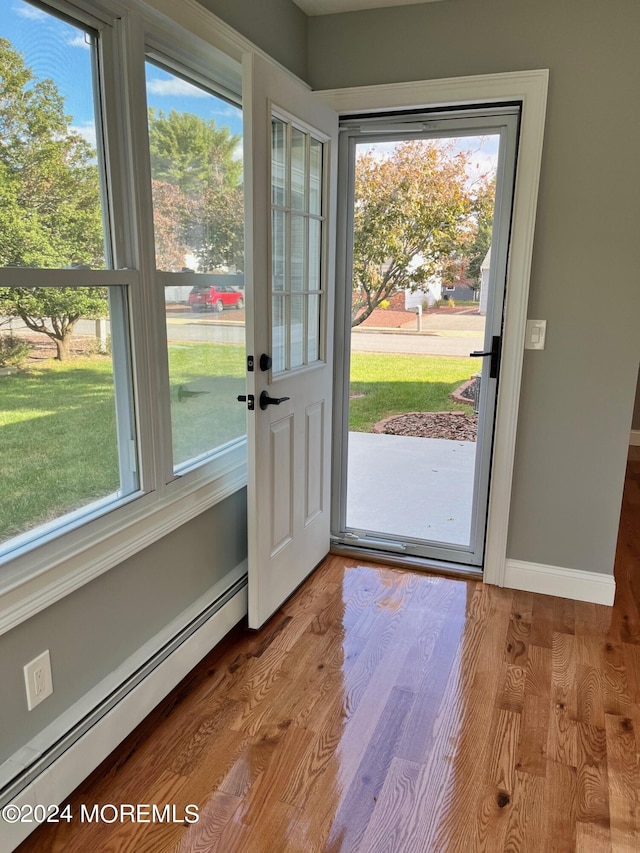 doorway featuring a wealth of natural light, baseboards, a baseboard heating unit, and wood finished floors