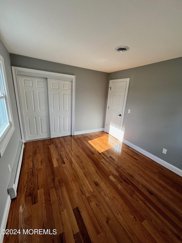 unfurnished bedroom with a closet, visible vents, baseboard heating, wood finished floors, and baseboards