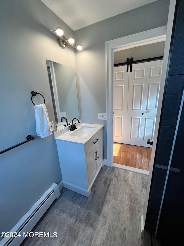 bathroom with a baseboard radiator, baseboards, wood finished floors, and vanity