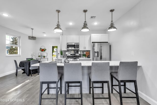 kitchen featuring a kitchen bar, appliances with stainless steel finishes, light wood-type flooring, decorative light fixtures, and white cabinetry