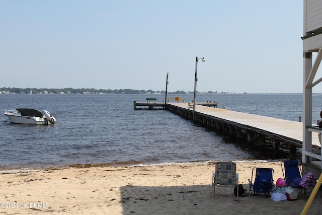 view of dock with a water view and a beach view