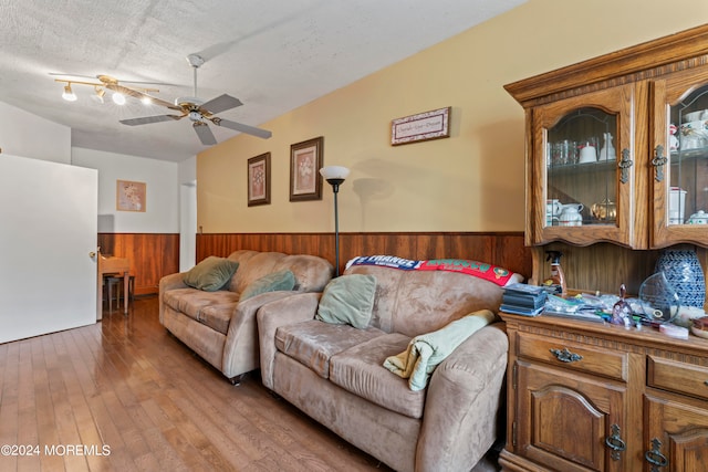 living room with ceiling fan, hardwood / wood-style flooring, a textured ceiling, and wood walls