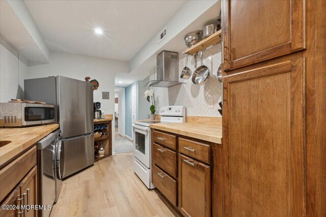 kitchen featuring wall chimney range hood, stainless steel appliances, light hardwood / wood-style floors, and wood counters