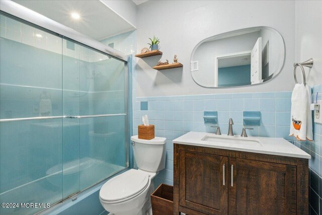 bathroom featuring vanity, walk in shower, toilet, and tile walls