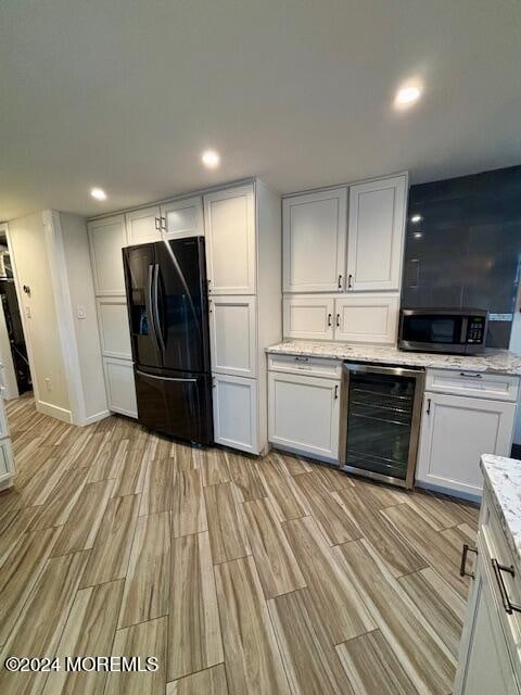 kitchen with wine cooler, white cabinets, black fridge, light hardwood / wood-style flooring, and light stone counters