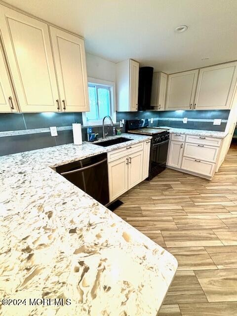 kitchen featuring sink, black appliances, light hardwood / wood-style flooring, and light stone counters