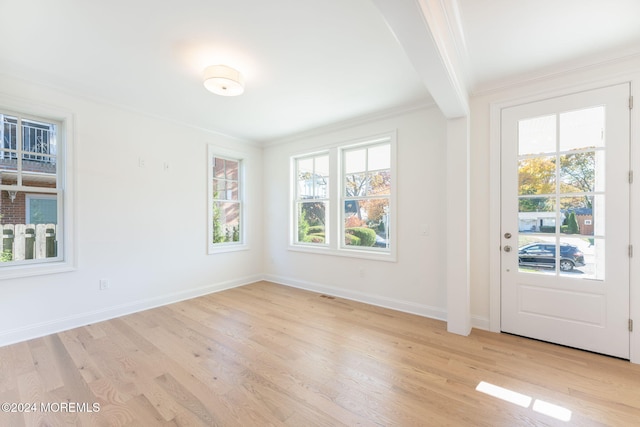 interior space featuring beamed ceiling, ornamental molding, and light hardwood / wood-style floors