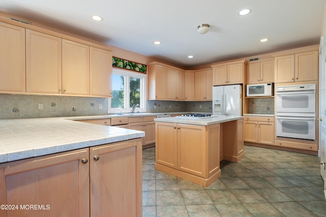 kitchen with light brown cabinets, tile counters, backsplash, a center island, and white appliances