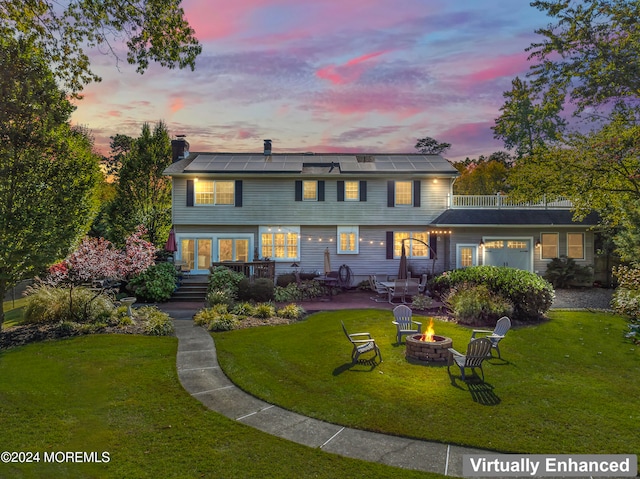 back house at dusk with a patio area, a yard, solar panels, and a fire pit