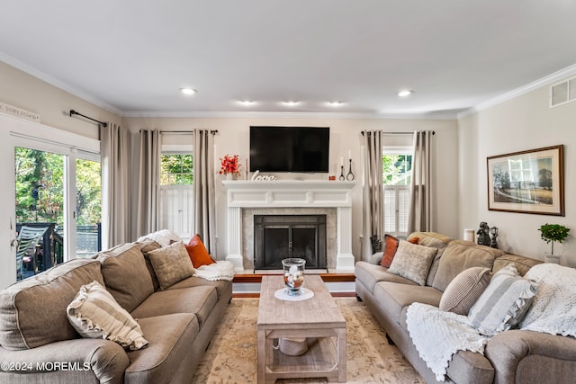 living room with ornamental molding, a healthy amount of sunlight, a tiled fireplace, and light wood-type flooring