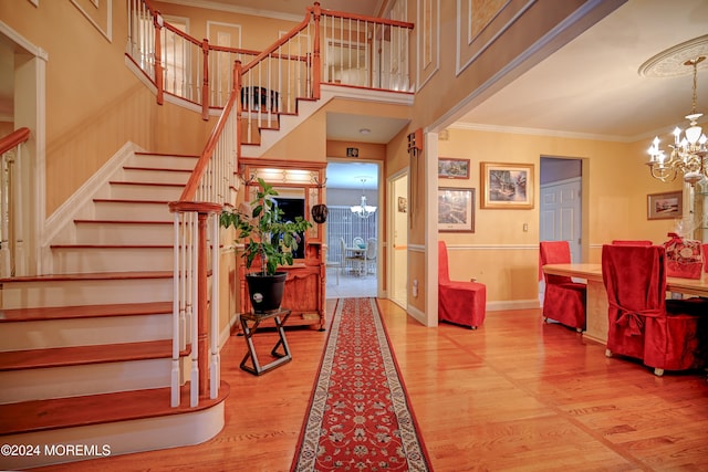 foyer with light hardwood / wood-style flooring, ornamental molding, a notable chandelier, and a high ceiling