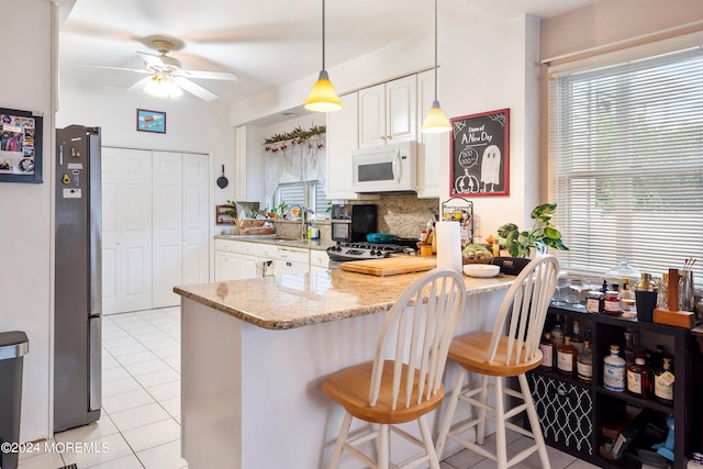 kitchen featuring tasteful backsplash, ceiling fan, appliances with stainless steel finishes, a breakfast bar, and light stone counters