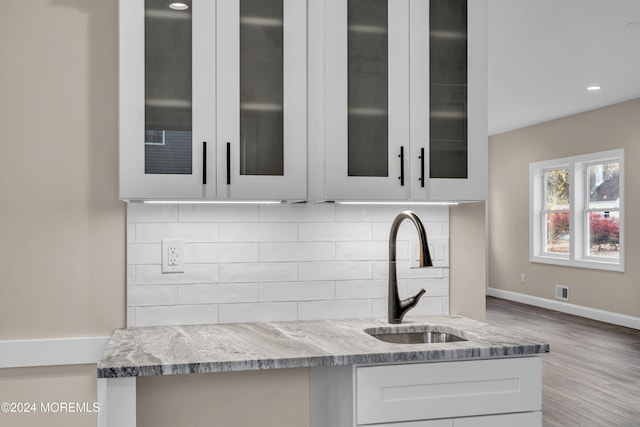 kitchen with light stone countertops, light wood-type flooring, backsplash, sink, and white cabinetry