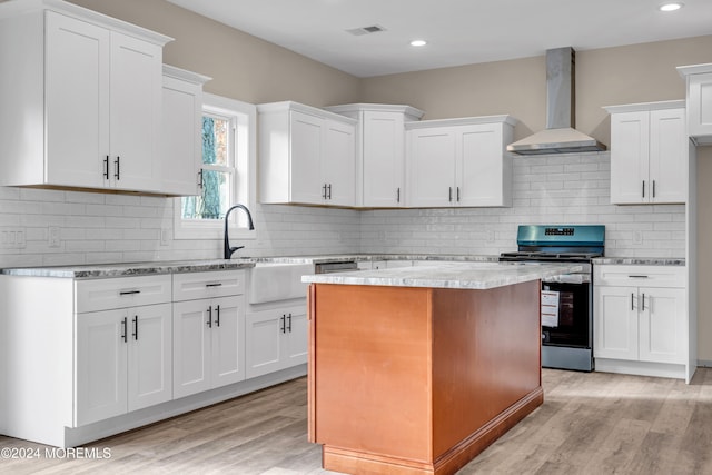 kitchen with white cabinets, wall chimney exhaust hood, stainless steel range oven, and light wood-type flooring