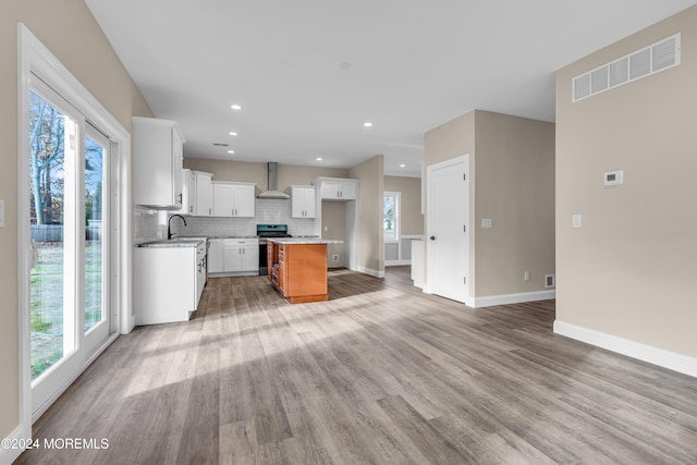 kitchen with a wealth of natural light, a kitchen island, wall chimney range hood, and stainless steel stove