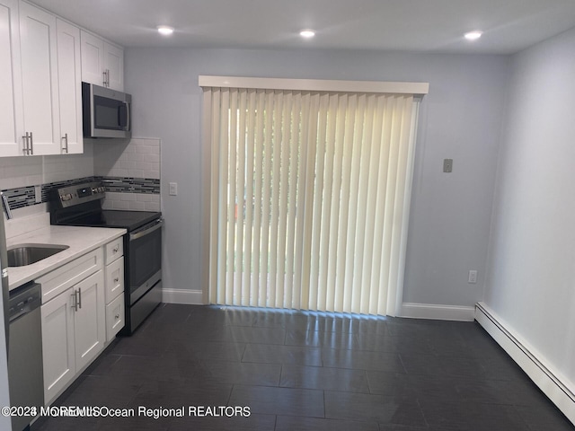 kitchen with appliances with stainless steel finishes, white cabinetry, a baseboard radiator, and backsplash