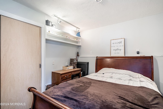 bedroom featuring rail lighting and a textured ceiling