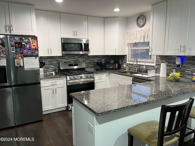 kitchen featuring stainless steel appliances, dark stone countertops, kitchen peninsula, a breakfast bar, and white cabinets