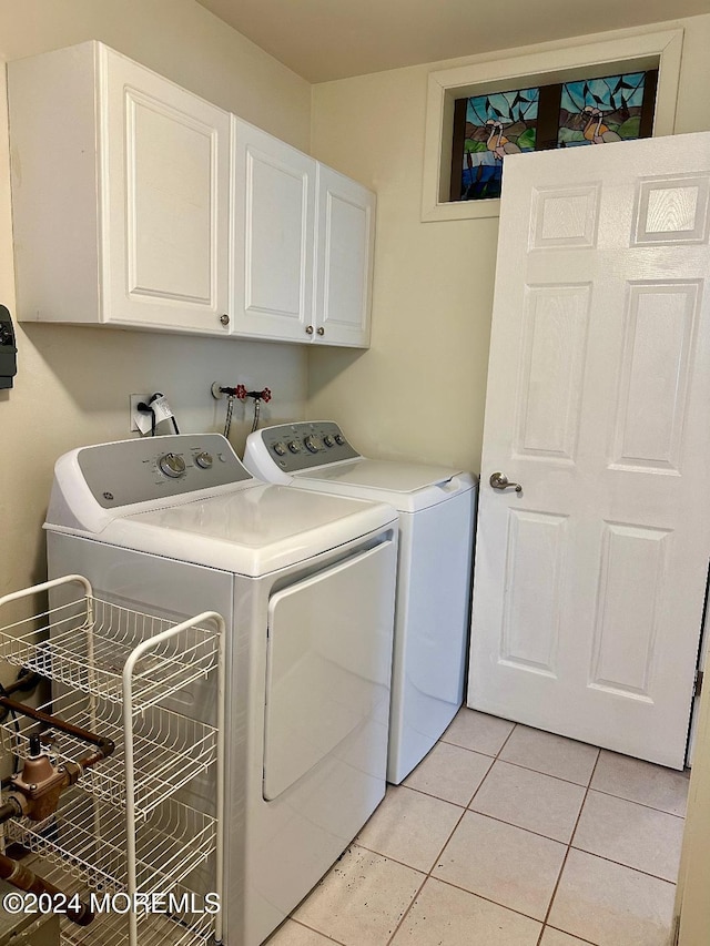 laundry area with separate washer and dryer, light tile patterned floors, and cabinets