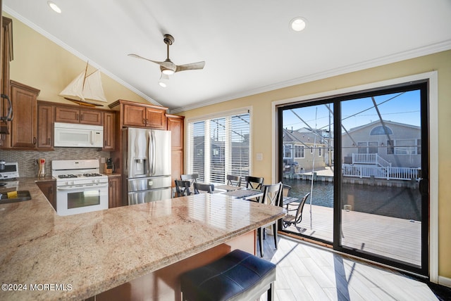 kitchen featuring white appliances, tasteful backsplash, kitchen peninsula, ornamental molding, and a breakfast bar area