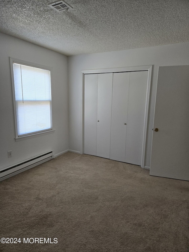 unfurnished bedroom with a closet, a textured ceiling, carpet floors, and baseboard heating