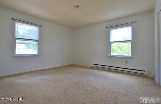 unfurnished room featuring a baseboard heating unit, a wealth of natural light, and light colored carpet