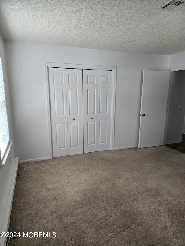 unfurnished bedroom featuring a closet, a baseboard heating unit, a textured ceiling, and dark carpet