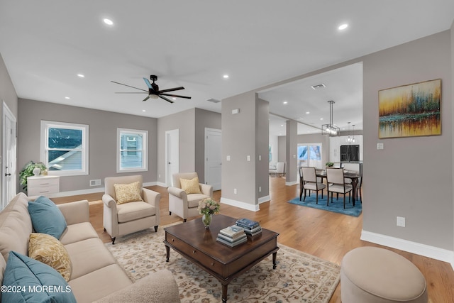 living room featuring ceiling fan with notable chandelier and light wood-type flooring