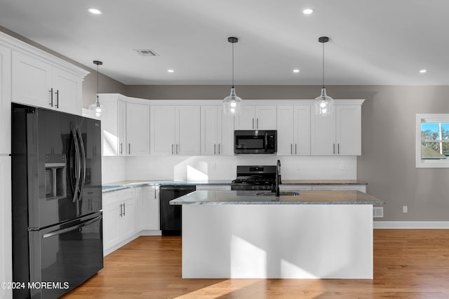 kitchen featuring black appliances, a center island with sink, and white cabinets