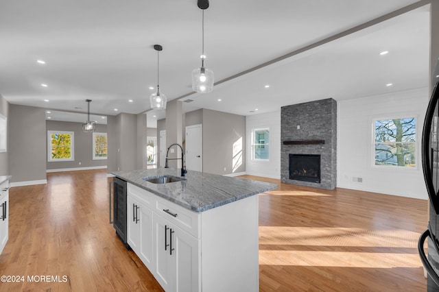 kitchen with sink, hanging light fixtures, light stone counters, light hardwood / wood-style floors, and white cabinets