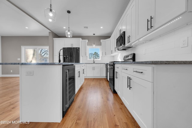 kitchen with a kitchen island with sink, black appliances, decorative light fixtures, light hardwood / wood-style floors, and white cabinetry