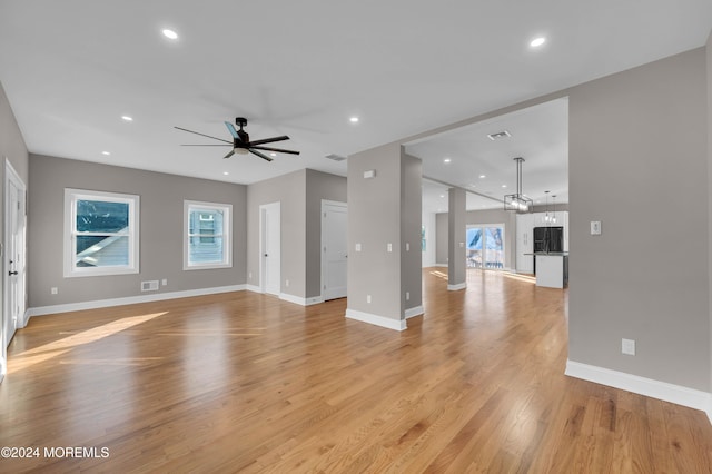 unfurnished living room with ceiling fan with notable chandelier and light hardwood / wood-style flooring