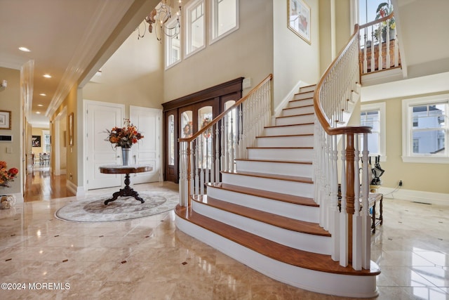 entryway featuring a healthy amount of sunlight, ornamental molding, a chandelier, and a towering ceiling