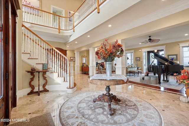 foyer entrance featuring ornate columns, crown molding, a towering ceiling, and ceiling fan