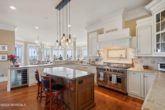 kitchen with kitchen peninsula, range with two ovens, wine cooler, a center island, and white cabinets