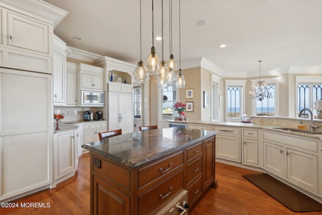 kitchen with stainless steel microwave, sink, a center island, white cabinetry, and decorative light fixtures