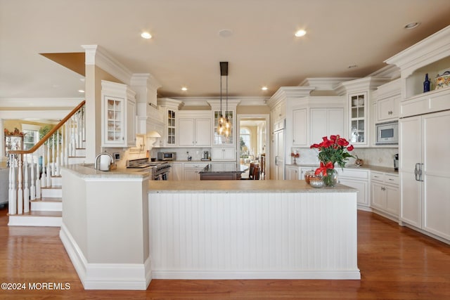 kitchen with kitchen peninsula, decorative backsplash, hardwood / wood-style flooring, crown molding, and stainless steel appliances