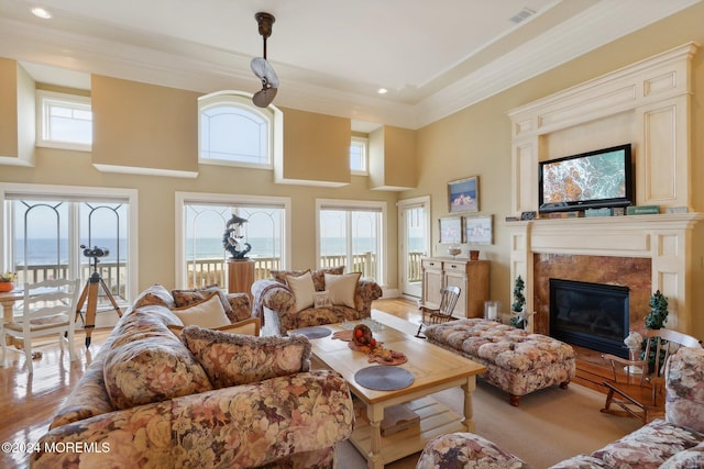 living room with a high end fireplace, crown molding, a water view, and a towering ceiling