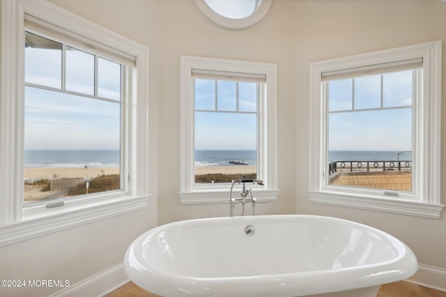 bathroom featuring a water view, a tub, and a view of the beach