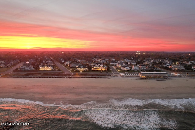 aerial view at dusk featuring a water view and a beach view