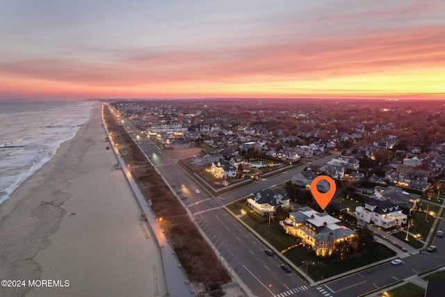 aerial view at dusk with a water view and a beach view